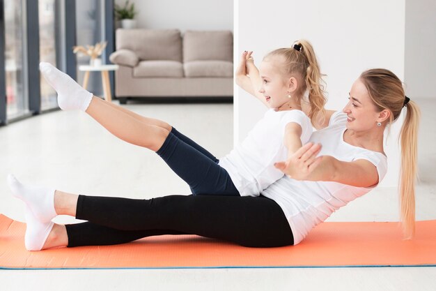 Vista laterale della madre che si esercita con la figlia a casa sulla stuoia di yoga