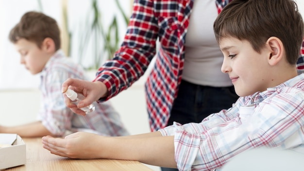 Vista laterale della madre disinfettante spray sulle mani del bambino