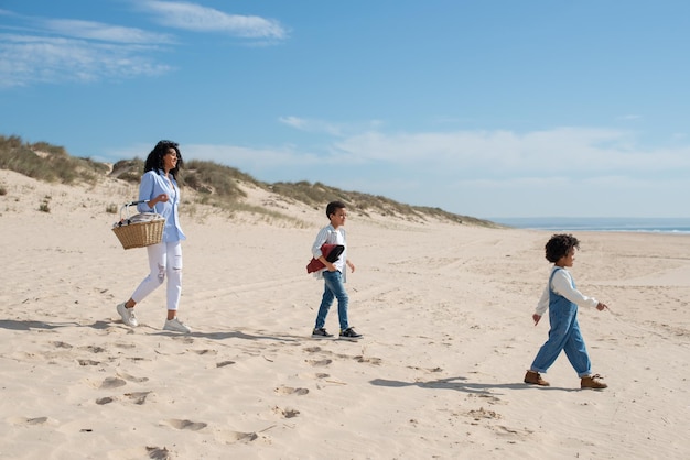Vista laterale della madre e dei bambini che camminano sulla spiaggia. Famiglia afroamericana che trascorre del tempo insieme all'aria aperta. Tempo libero, tempo in famiglia, concetto di genitorialità