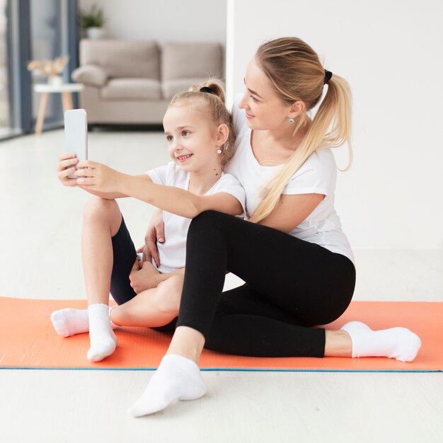 Vista laterale della madre e della figlia che prendono selfie sulla stuoia di yoga