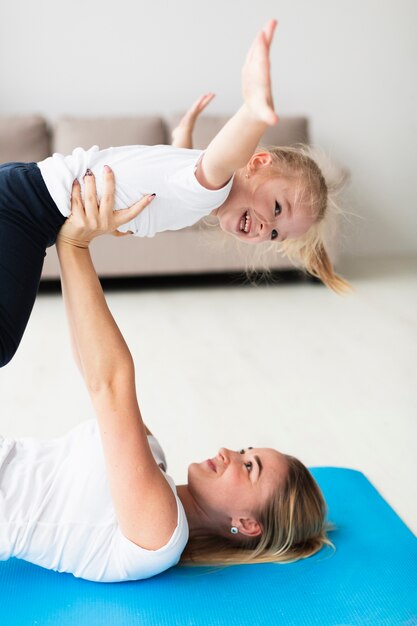 Vista laterale della madre sulla stuoia di yoga che alza figlia felice