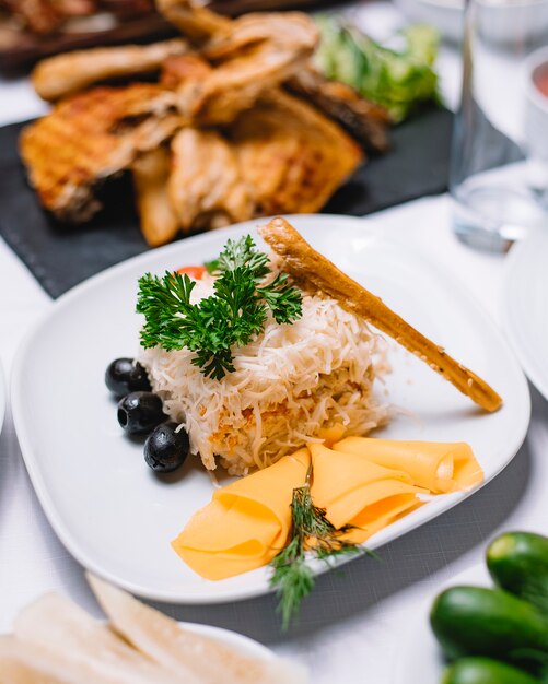 Vista laterale della mimosa russa tradizionale insalata con patate pesce cannad formaggio carote e uova decorate con olive nere ed erbe fresche su un piatto bianco