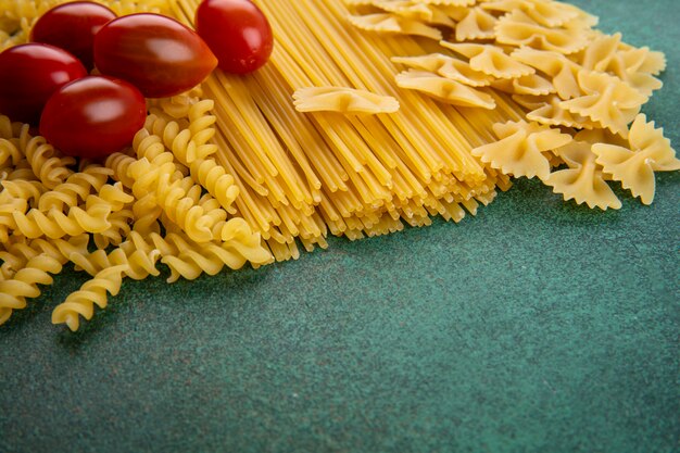 Vista laterale della pasta cruda con spaghetti crudi e pomodorini su una superficie verde