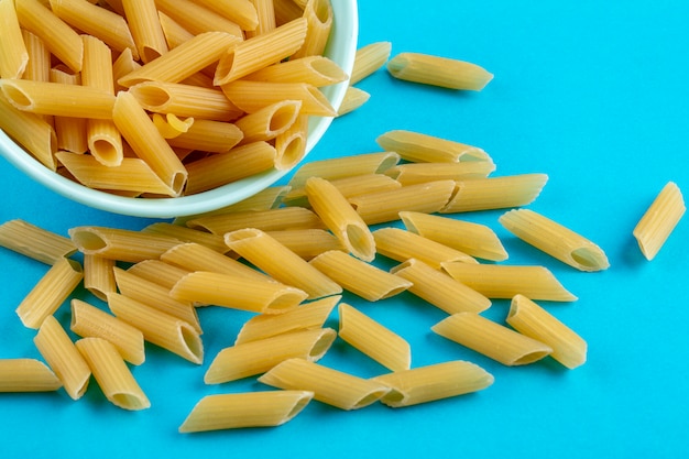 Vista laterale della pasta cruda in un piattino su una superficie blu