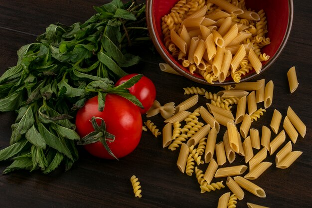 Vista laterale della pasta cruda in una ciotola con pomodori e menta su una superficie di legno