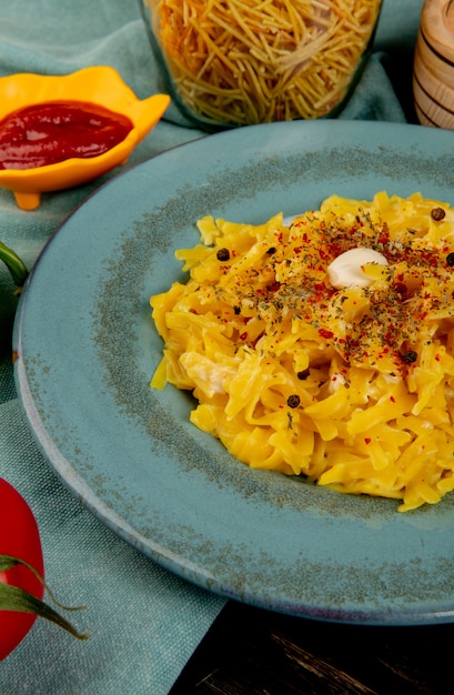 Vista laterale della pasta di maccheroni in zolla con il pomodoro degli spaghetti del ketchup sul panno blu e sulla tabella di legno