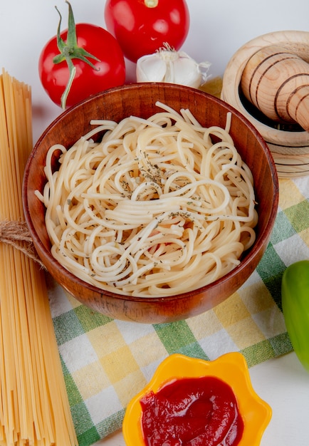 Vista laterale della pasta maccheroni in una ciotola con pomodori pepe nero aglio ketchup pepe e vermicelli sul panno plaid