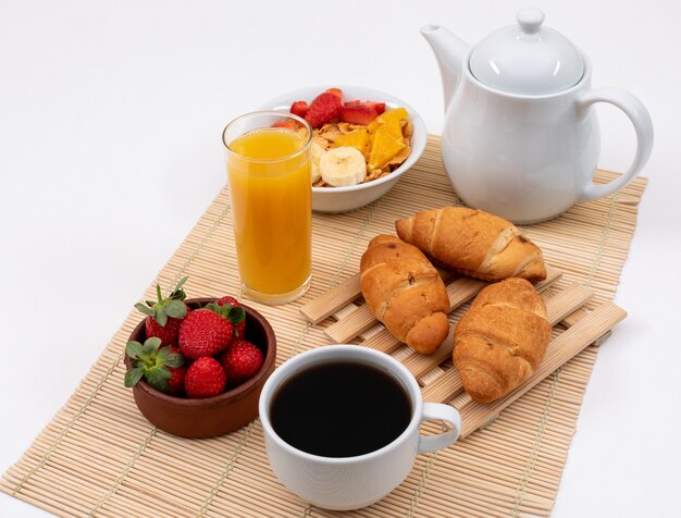 Vista laterale della prima colazione con i fiocchi di granturco, le fragole, il succo ed i croissant sull'orizzontale di superficie di bianco