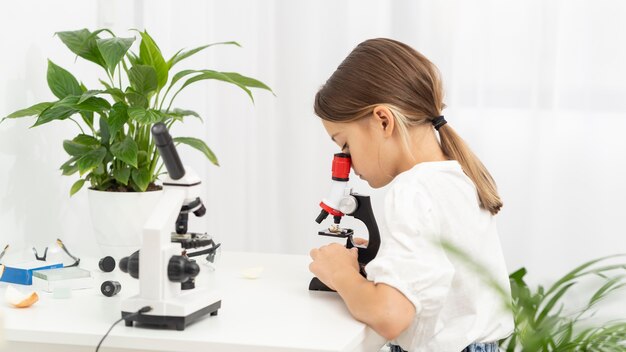Vista laterale della ragazza che esamina il microscopio