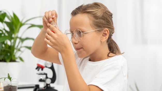 Vista laterale della ragazza che impara a conoscere la scienza con il microscopio