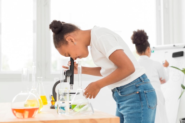 Vista laterale della ragazza che osserva tramite il microscopio