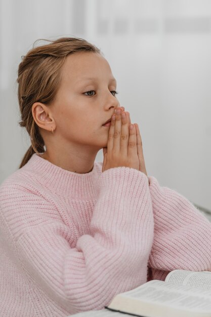 Vista laterale della ragazza che prega con la Bibbia