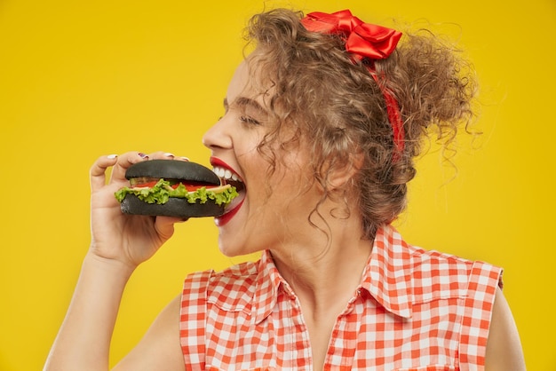 Vista laterale della ragazza felice che cerca di mangiare hamburger nero