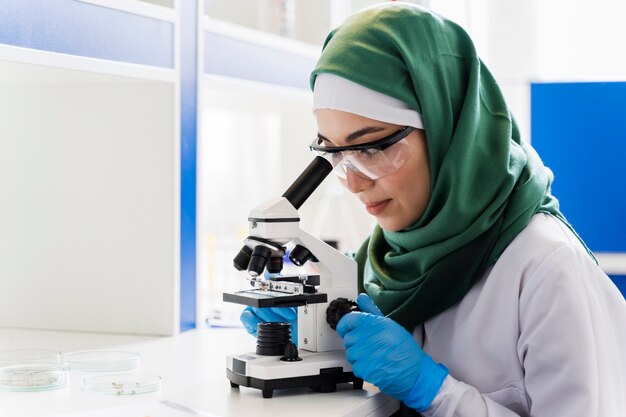Vista laterale della scienziata con hijab e microscopio