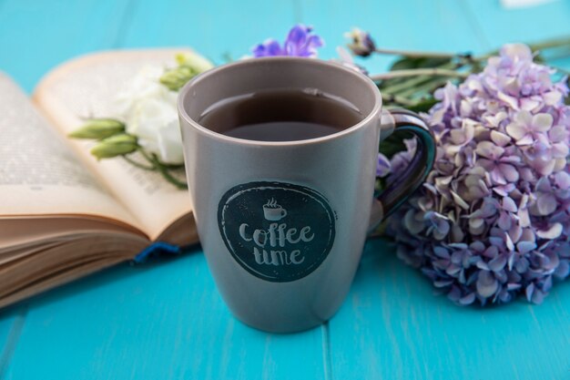 Vista laterale della tazza di caffè con fiori e libro aperto su sfondo blu