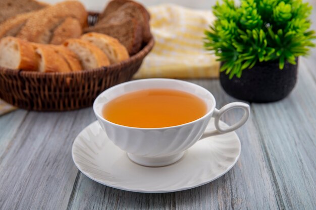 Vista laterale della tazza di toddy caldo sul piattino con fette di pane nel cestino su un panno plaid e pianta su fondo in legno