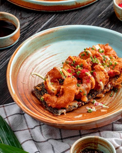 Vista laterale della tempura fritta dei gamberetti con le cipolle verdi e la salsa tritate su un piatto su legno