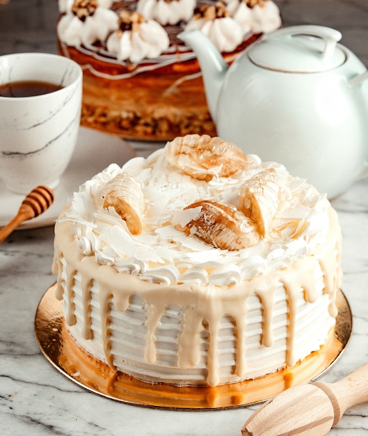 Vista laterale della torta bianca decorata con panna montata fusa e banane sul tavolo