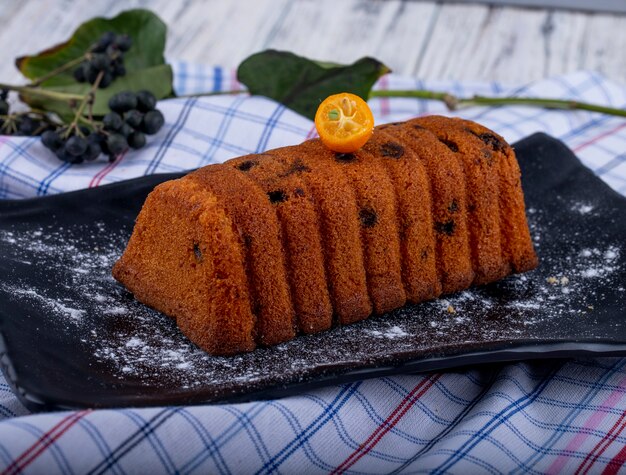 Vista laterale della torta con uvetta decorata con fetta di kumquat e zucchero a velo su un bordo nero