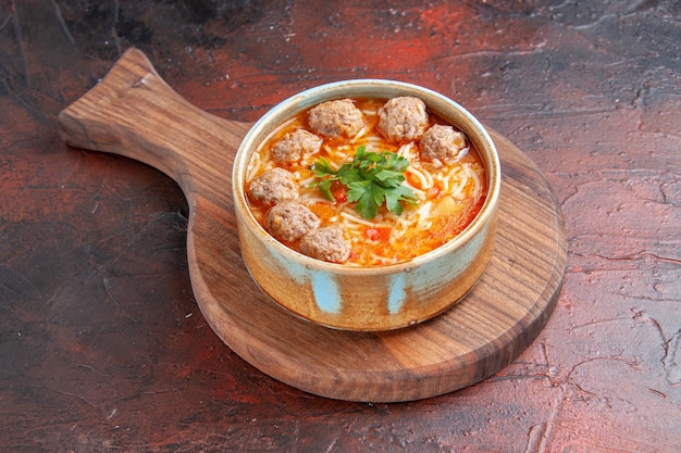 Vista laterale della zuppa di polpette di pomodoro con noodles in una ciotola marrone su sfondo scuro