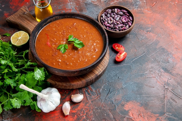 Vista laterale della zuppa di pomodoro su un tagliere marrone e fagioli su una tavola di colori misti