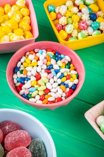 Vista laterale delle caramelle di zucchero dolci variopinte in ciotole su fondo di legno verde