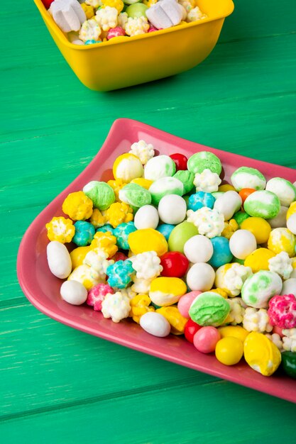 Vista laterale delle caramelle di zucchero dolci variopinte in ciotole su fondo di legno verde