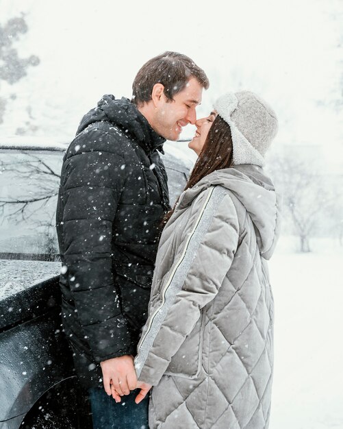 Vista laterale delle coppie di smiley che baciano nella neve durante un viaggio su strada