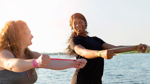Vista laterale delle donne che esercitano con elastici in riva al lago