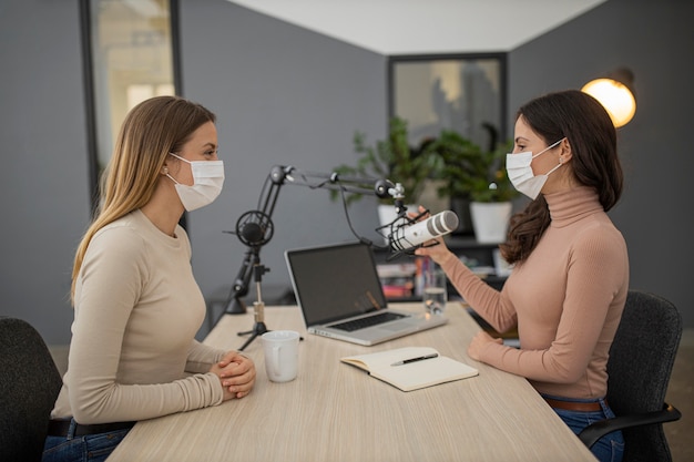 Vista laterale delle donne con maschere mediche che trasmettono insieme alla radio