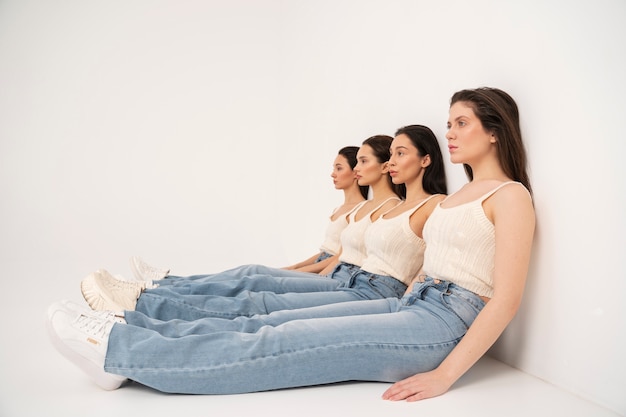 Vista laterale delle donne in canottiere e jeans seduti contro il muro