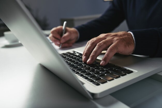 Vista laterale delle mani maschii che scrivono sulla tastiera del computer portatile