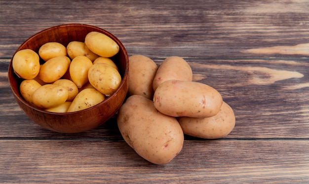 Vista laterale delle patate novelle in ciotola e quelle bianche sulla tavola di legno con lo spazio della copia