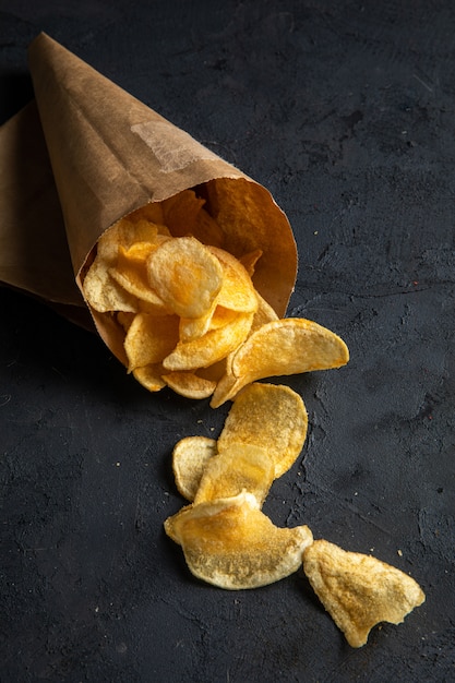 Vista laterale delle patatine fritte sparse da una borsa di pepe sul nero