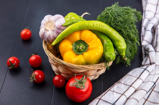 Vista laterale delle verdure come merce nel carrello dell'aneto dell'aglio del pepe con i pomodori e il panno del plaid sul nero