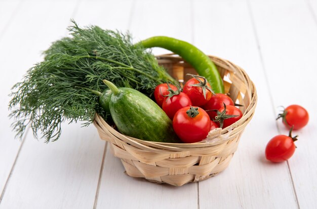 Vista laterale delle verdure come merce nel cestino del cetriolo dell'aneto del pomodoro su legno