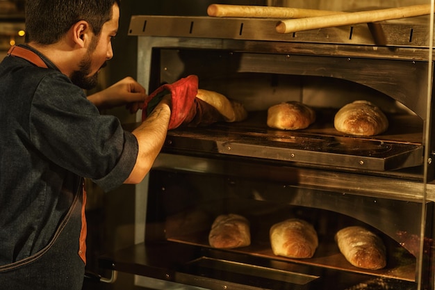 Vista laterale dello chef professionista che cucina deliziosa bistecca di manzo succosa sulla griglia fiammeggiante bell'uomo con barba e tatuaggi a portata di mano che prepara il cibo nella moderna cucina del ristorante