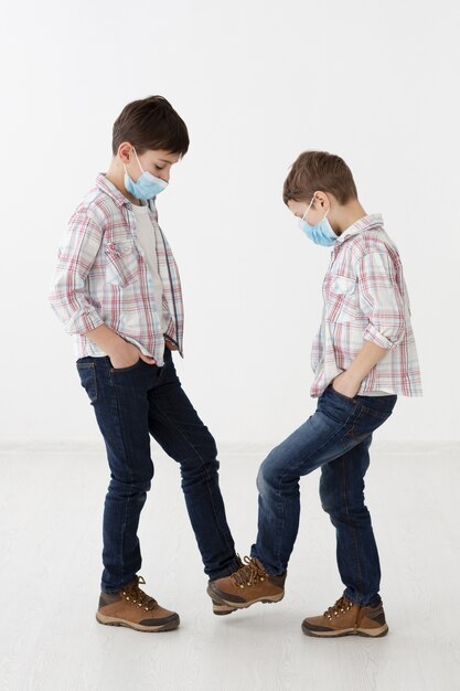 Vista laterale di bambini con maschere mediche che mostrano saluti senza contatto