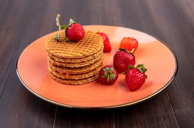 Vista laterale di biscotti waffle con fragole nel piatto su legno