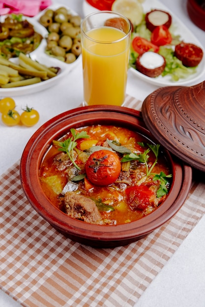 Vista laterale di carne in umido con patate e pomodori in una pentola di terracotta