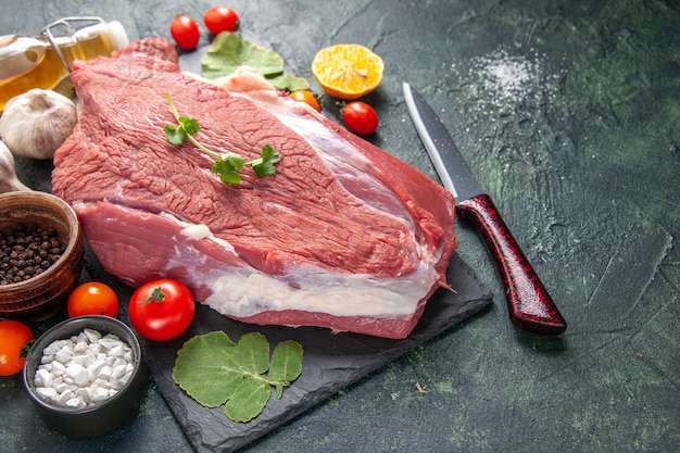 Vista laterale di carne rossa cruda fresca su vassoio nero verdure al pepe coltello da bottiglia di olio caduto su sfondo di colore scuro