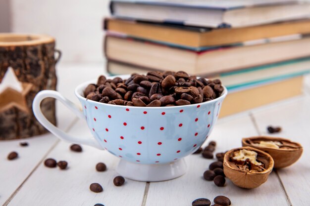 Vista laterale di chicchi di caffè tostati freschi su una tazza a pois con noce su un fondo di legno bianco