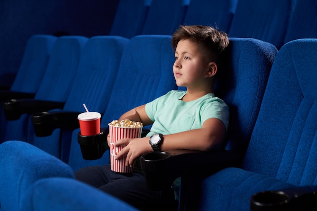 Vista laterale di cibo spazzatura mangiante teenager maschio rilassato in cinema