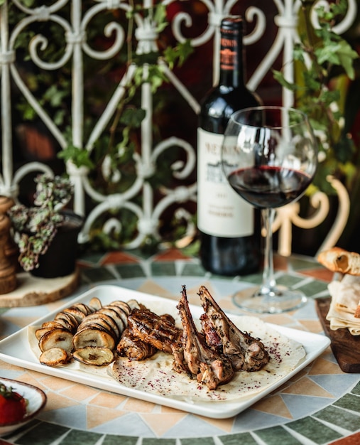 Vista laterale di costolette di agnello alla griglia con carne di manzo e patate al forno a fette sul tavolo servito con bottiglia di vino