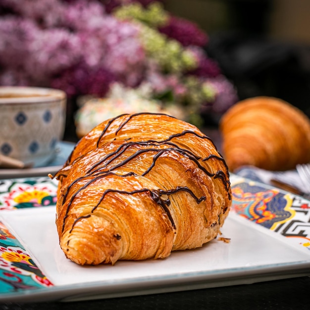 Vista laterale di croissant al cioccolato su piatto bianco con sfondo di fiori viola