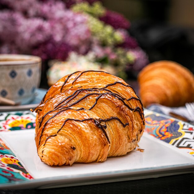 Vista laterale di croissant al cioccolato su piatto bianco con sfondo di fiori viola