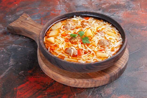 Vista laterale di deliziosa zuppa di noodle con pollo su tagliere di legno su sfondo scuro