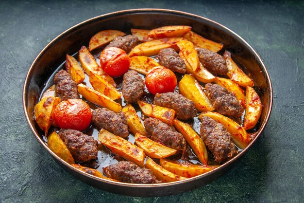 Vista laterale di deliziose cotolette di carne al forno con patate e pomodori su sfondo di colore verde e nero mix