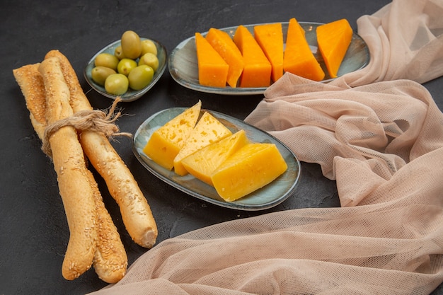 Vista laterale di fette di formaggio fresco e gustoso su un asciugamano e olive verdi su sfondo nero