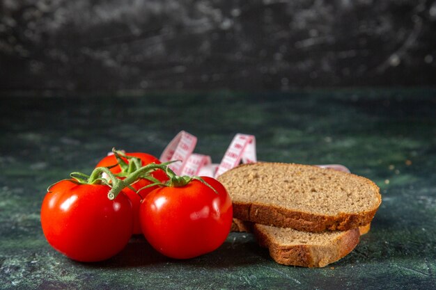 Vista laterale di fette di pane nero pomodori freschi con gambo e metri su sfondo di colori scuri